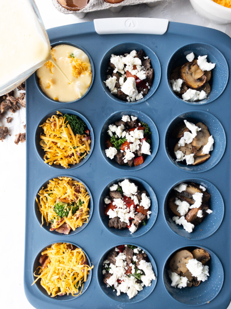 Egg custard being poured into one cup of a blue silicone muffin tin for homemade egg bites.