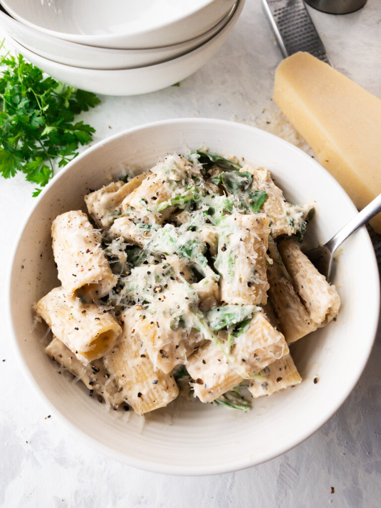 A serving of pasta bianca (white pasta) in cream sauce with arugula, parmesan, and pepper in a white bowl.