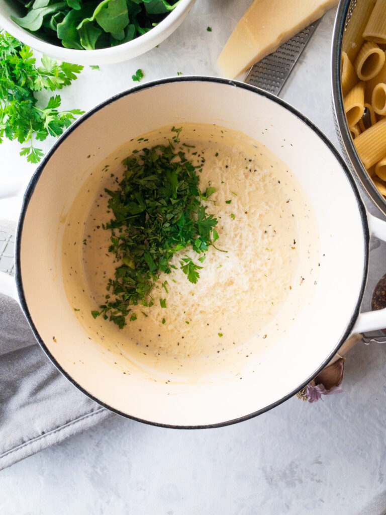 Pasta cream sauce with fresh parsley and parmesan in a white dutch oven.