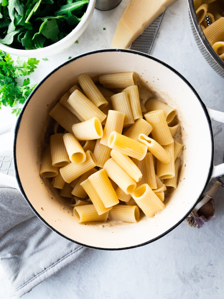 Cooked rigatoni pasta on top of a white cream sauce in a white pot.