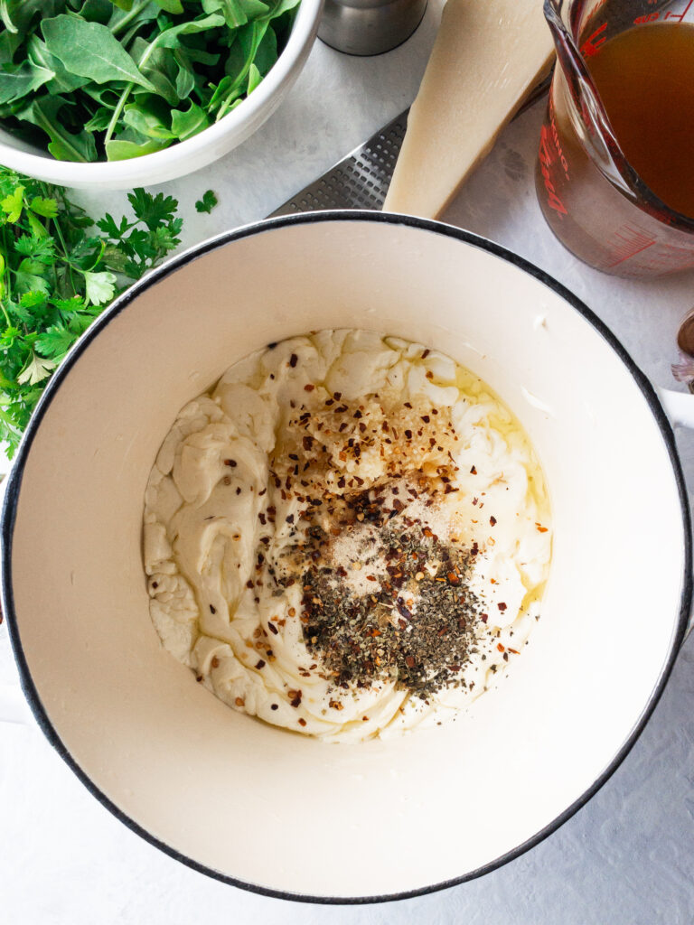 Cream cheese-based pasta sauce with melted butter, dried herbs, and garlic in a white pot.