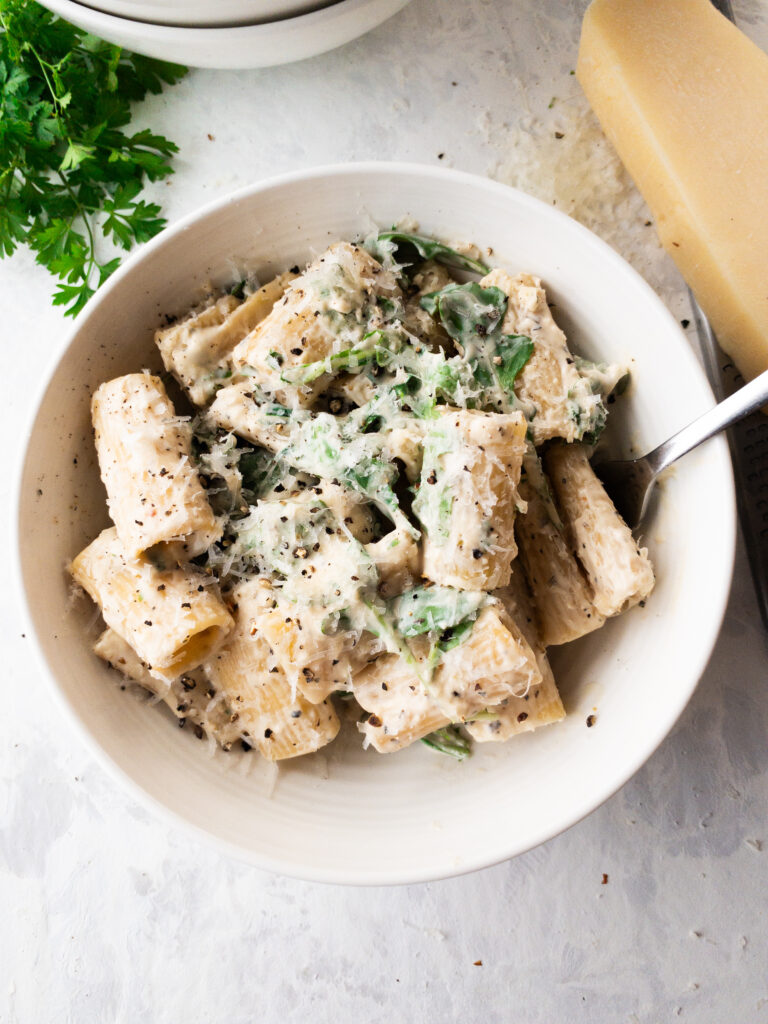 Rigatoni pasta in a garlic cream sauce topped with arugula.