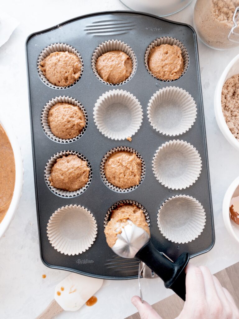 Pumpkin muffin batter being spooned into muffin cups.