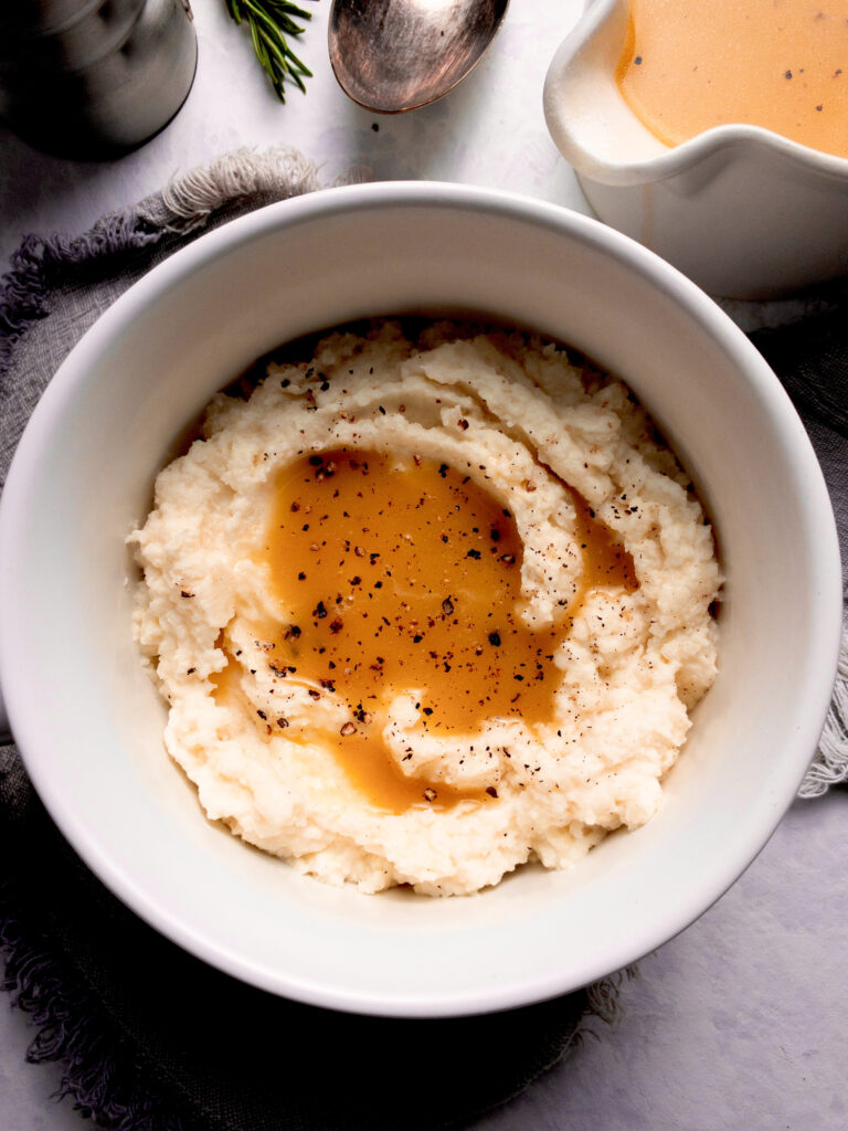 Low carb gravy poured over creamy cauliflower mashed potatoes for a keto-friendly holiday side dish.
