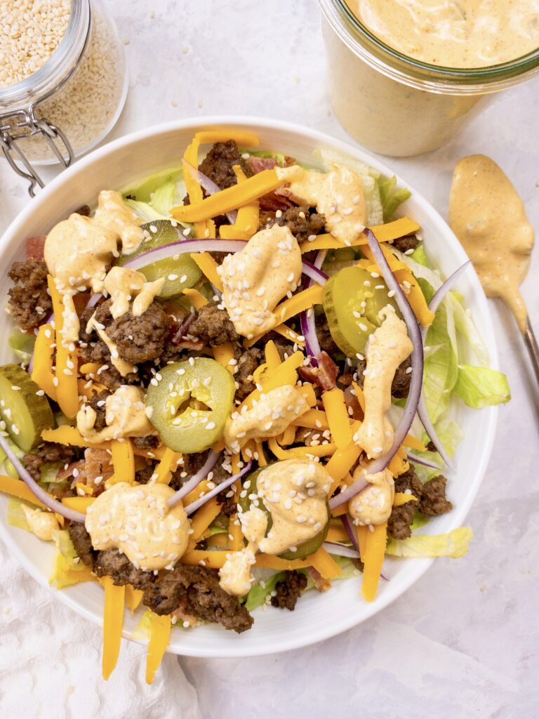Homemade Big Mac Salad made with iceberg lettuce, seasoned ground beef, shredded cheddar cheese, sliced red onion, crumbled bacon, and pickles topped with Copycat Big Mac sauce and sesame seeds.