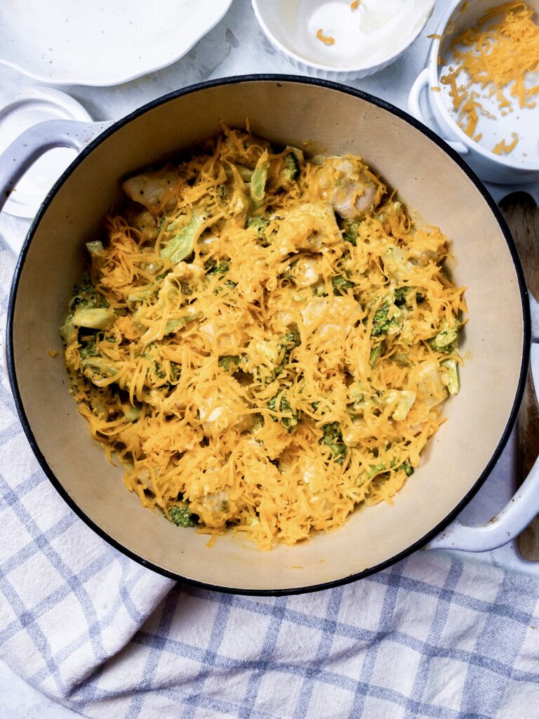 One-pan chicken broccoli casserole topped with shredded cheddar cheese, before baking.